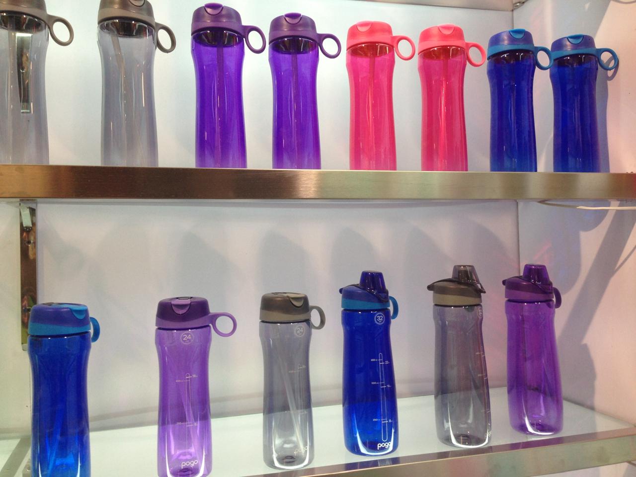 Botellas deportivas de plástico reutilizable exhibidas en estantes, en varios colores (azul, violeta, rosa y gris).